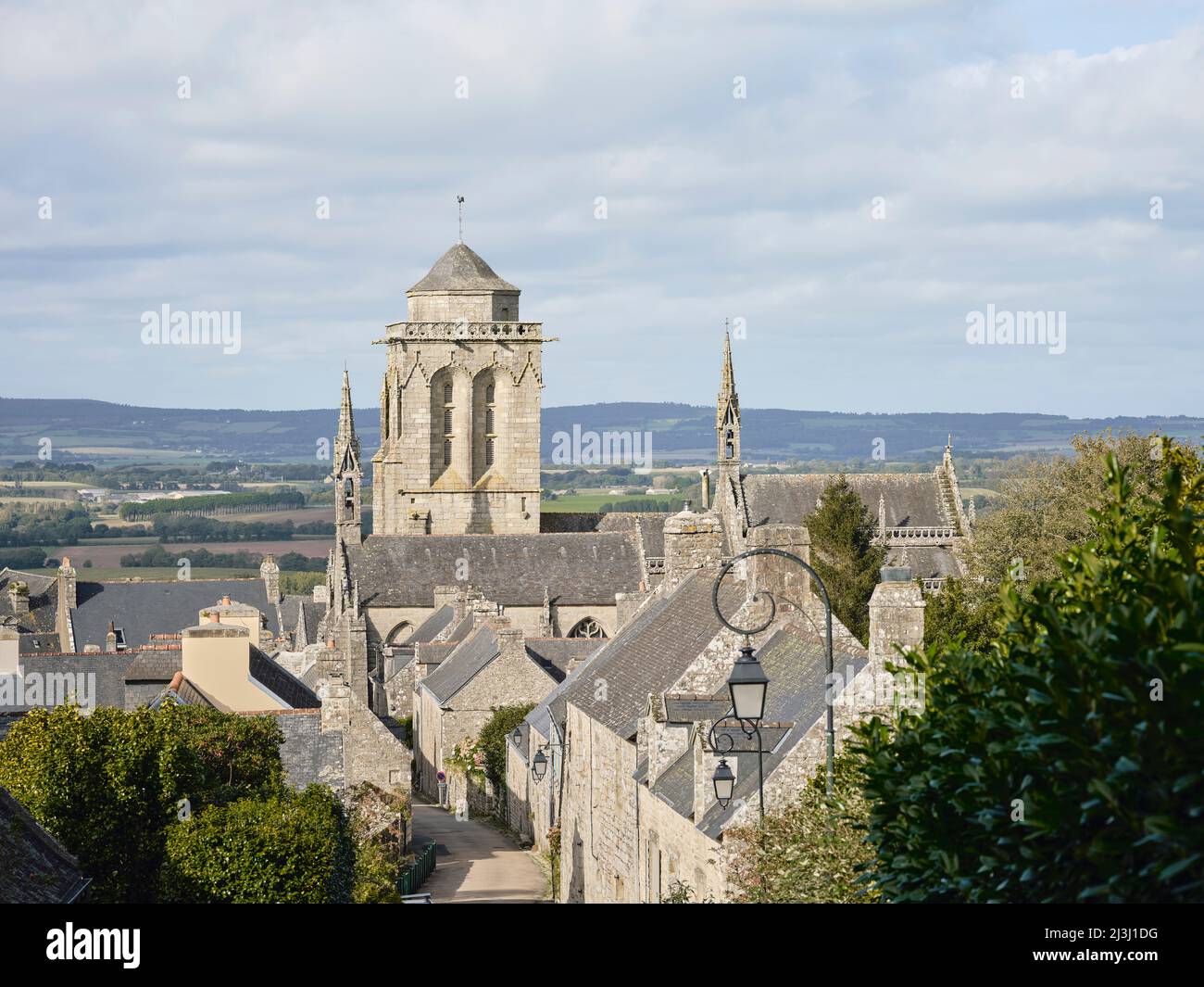 The tower of the Église Saint-Ronan in the village of Locronan in the department of Finistère in Brittany. The cottages were built of granite and date back to the 17th century. Locronan's historic setting has been featured in many film and television productions. Locronan is a popular destination for excursions. Stock Photo
