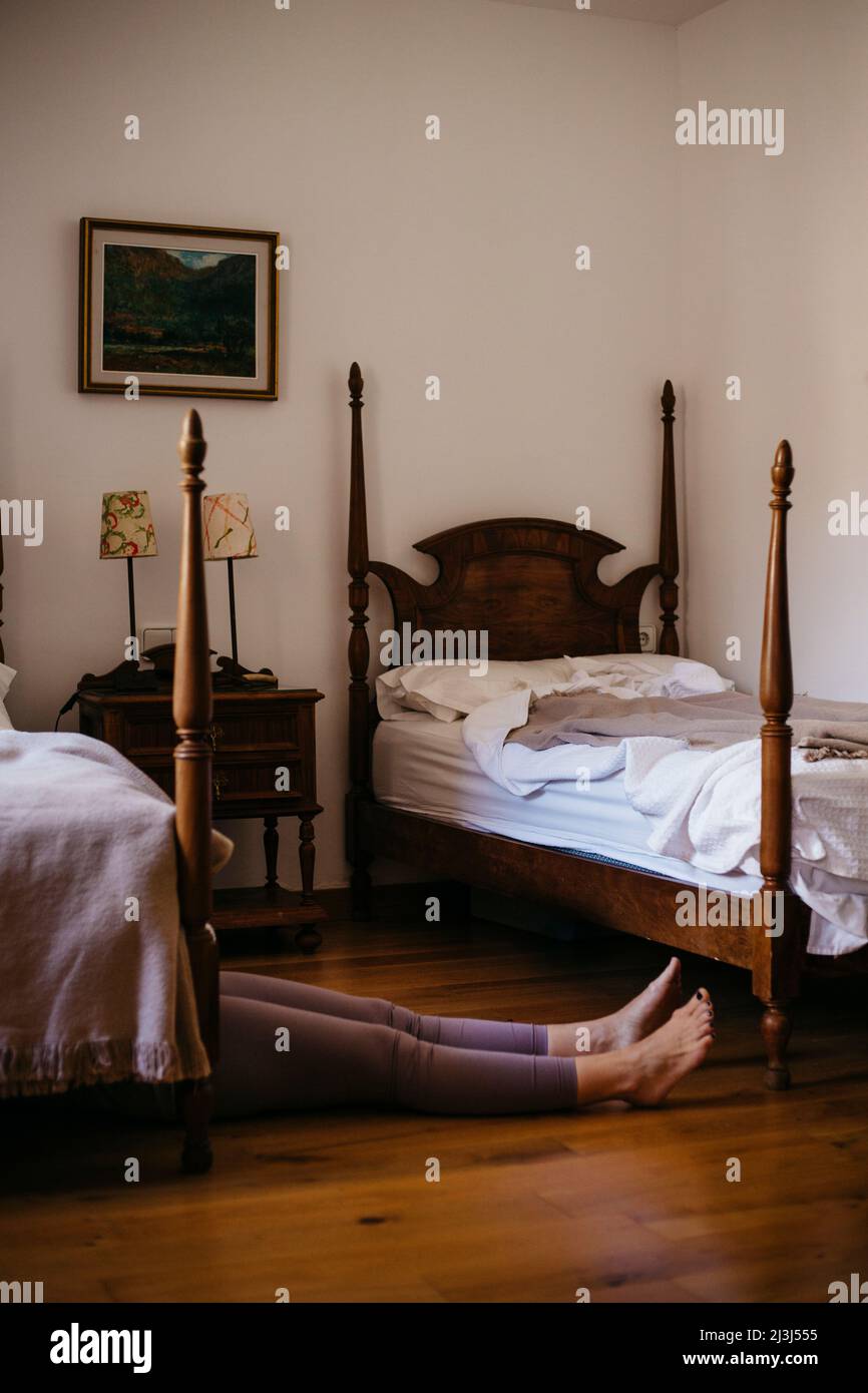 Woman lying half under a bed in a small bedroom Stock Photo