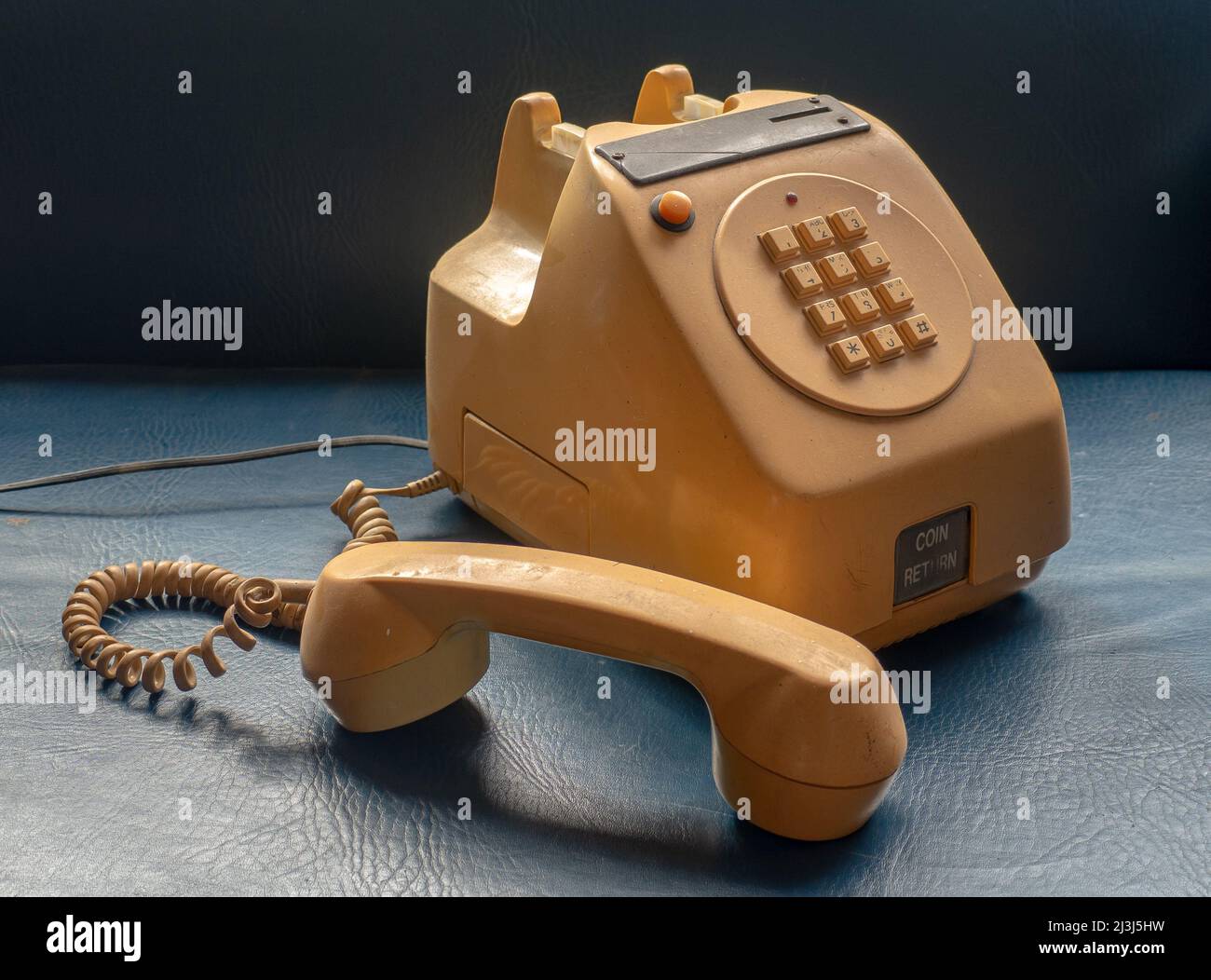 Old table version coin-operated public telephone, the kind used in bars and shops, yellow on a blue background. Stock Photo