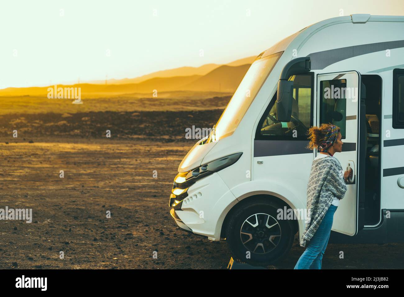 Woman alone traveler enjoy outdoor leisure activity traveling with a big modern camper motor home van rv. Beautiful sunset in background. Freedom and Stock Photo