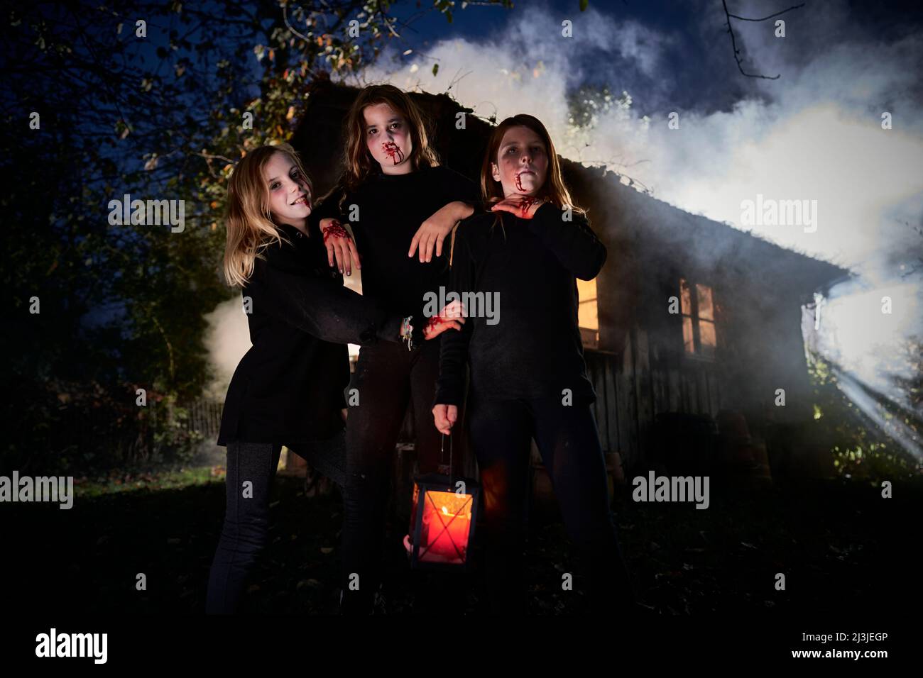3 young girls with Halloween costumes in front of hut, in fog Stock Photo