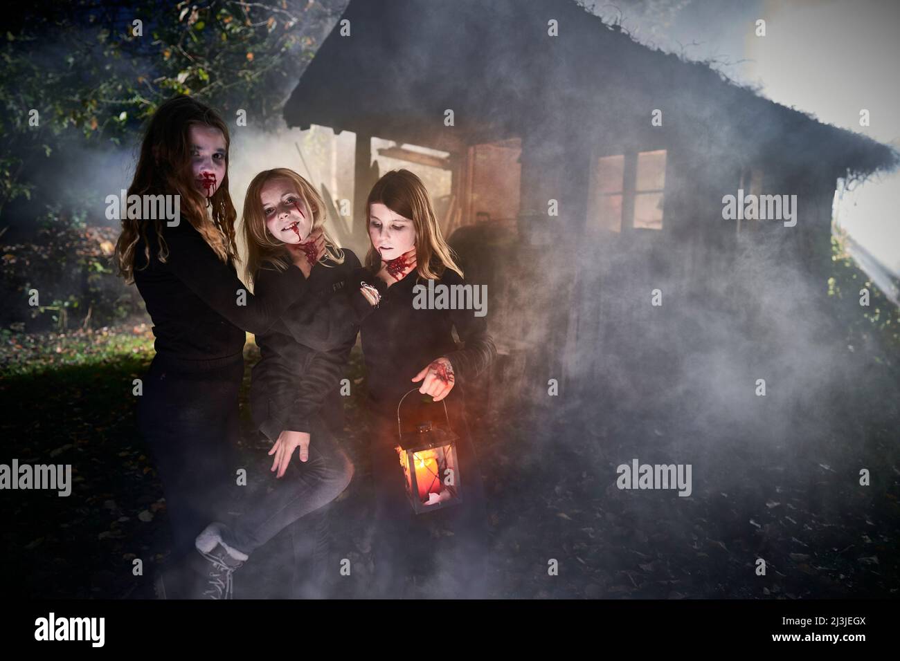 3 young girls with Halloween costumes in front of hut, in fog Stock Photo