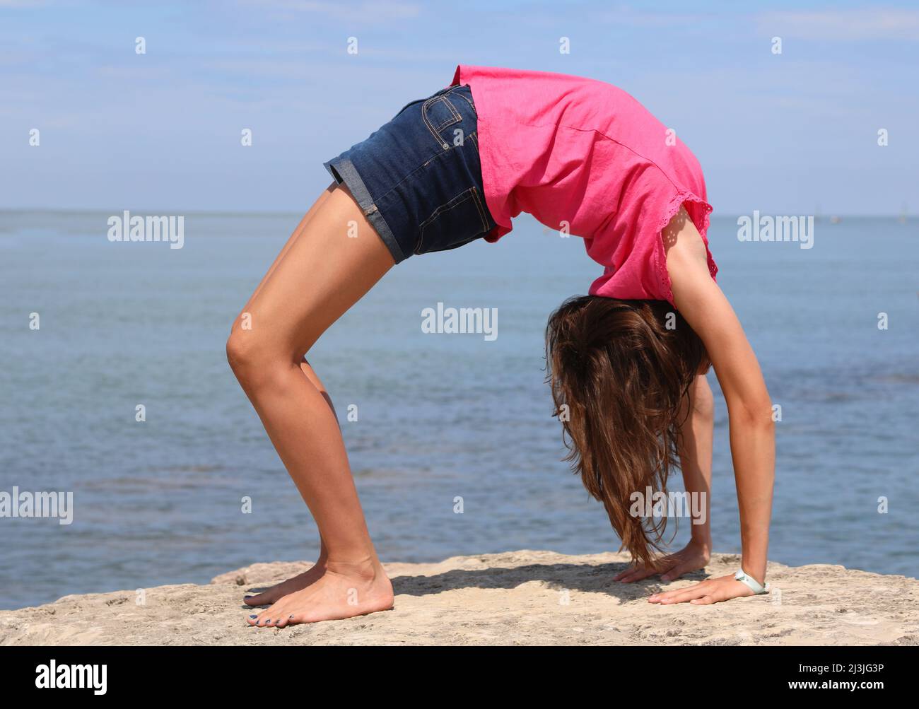 slender and articulated girl while performing a bridge by turning her back backwards by the sea Stock Photo