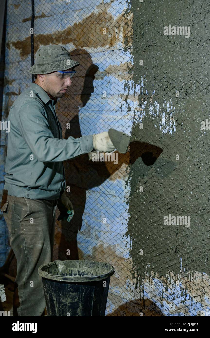 First Layer Plaster A man throws concrete mortar on the wall, the first layer of plaster on ...