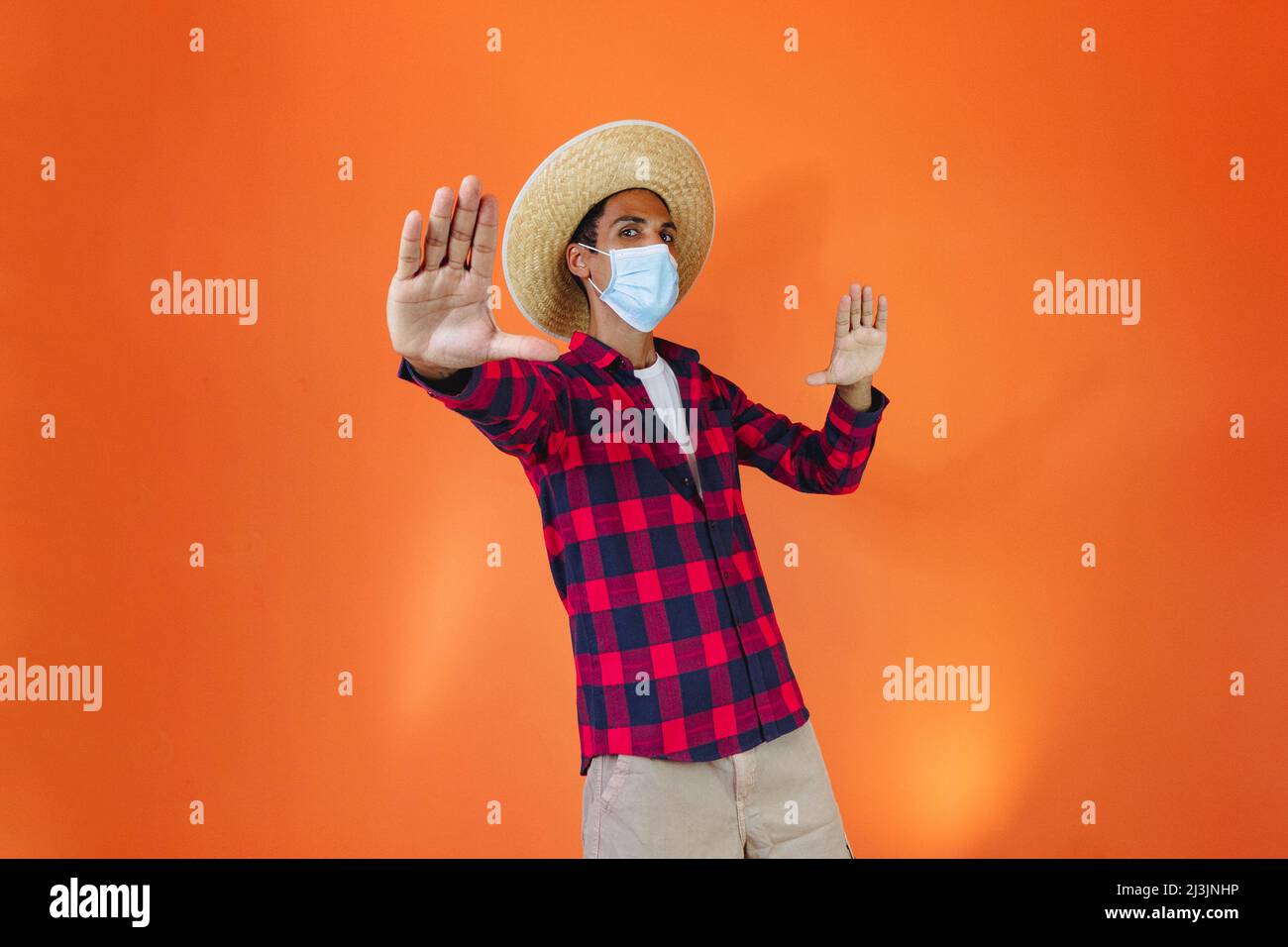 Black Man With Junina Party Outfit and pandemic mask Isolated on Orange Background. Young man wearing traditional clothes for Festa Junina - Brazilian Stock Photo