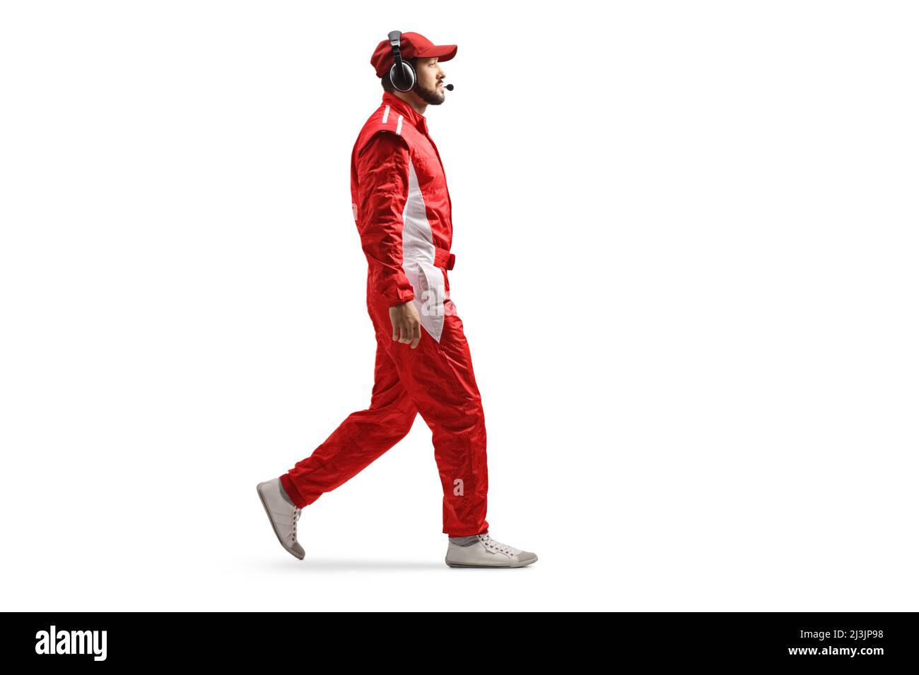Full length profile shot of a race team member with headphones and a red suit walking isolated on white background Stock Photo