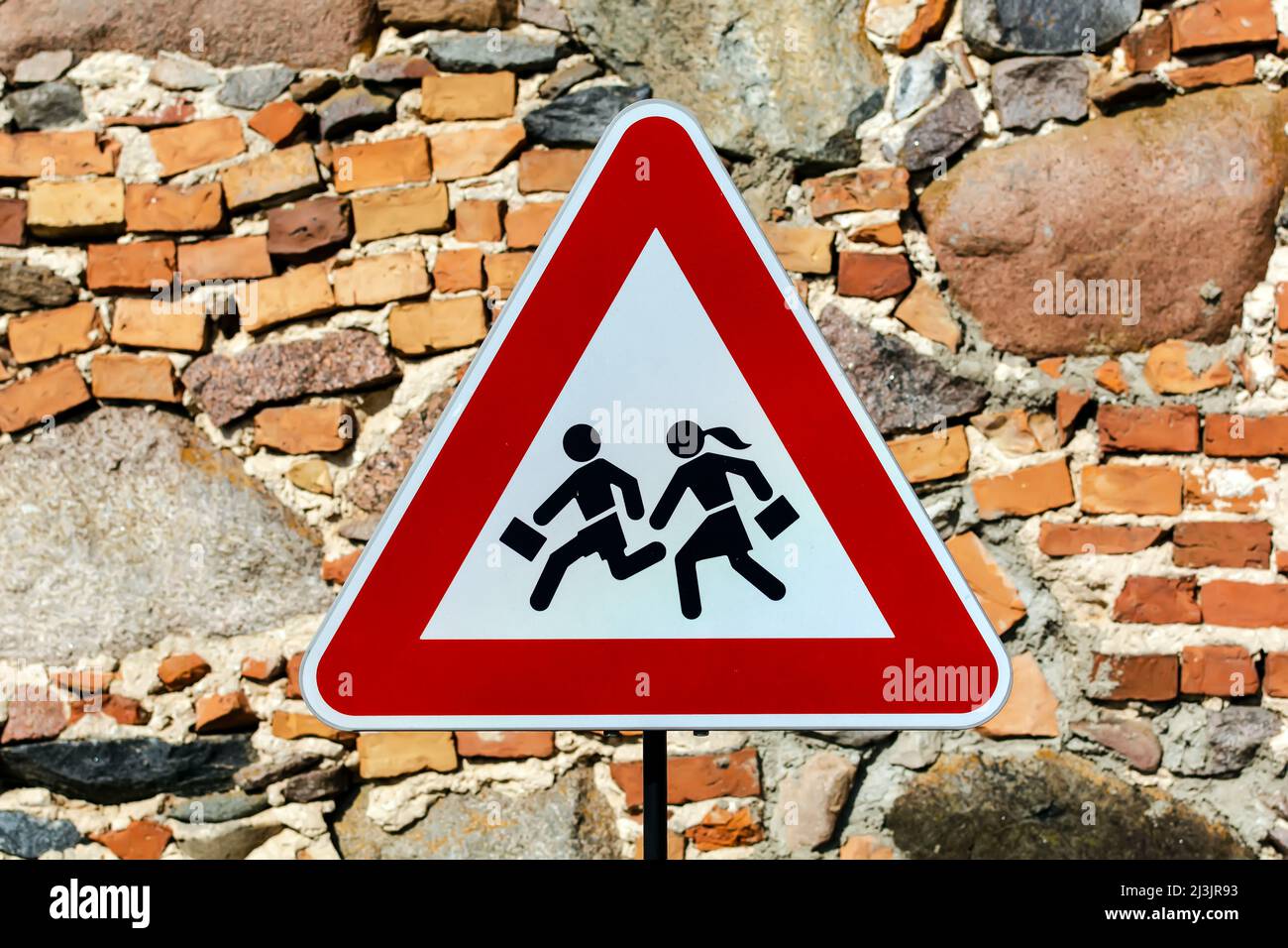 Triangular warning 'children crossing' school road traffic sign with stone masonry wall behind Stock Photo