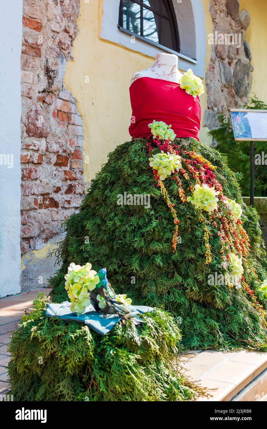 Evening gown made of evergreen Thuja branches and decorated with yellow flowers and red berries. Stock Photo