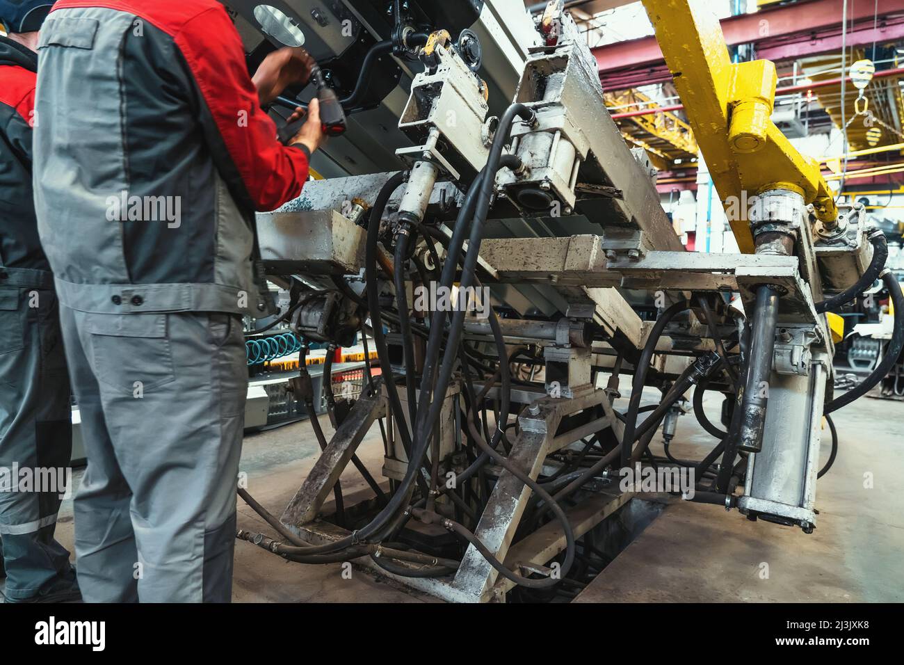 Workers at farm machinery factory assemble spare parts on special machine tool in workplace. Stock Photo