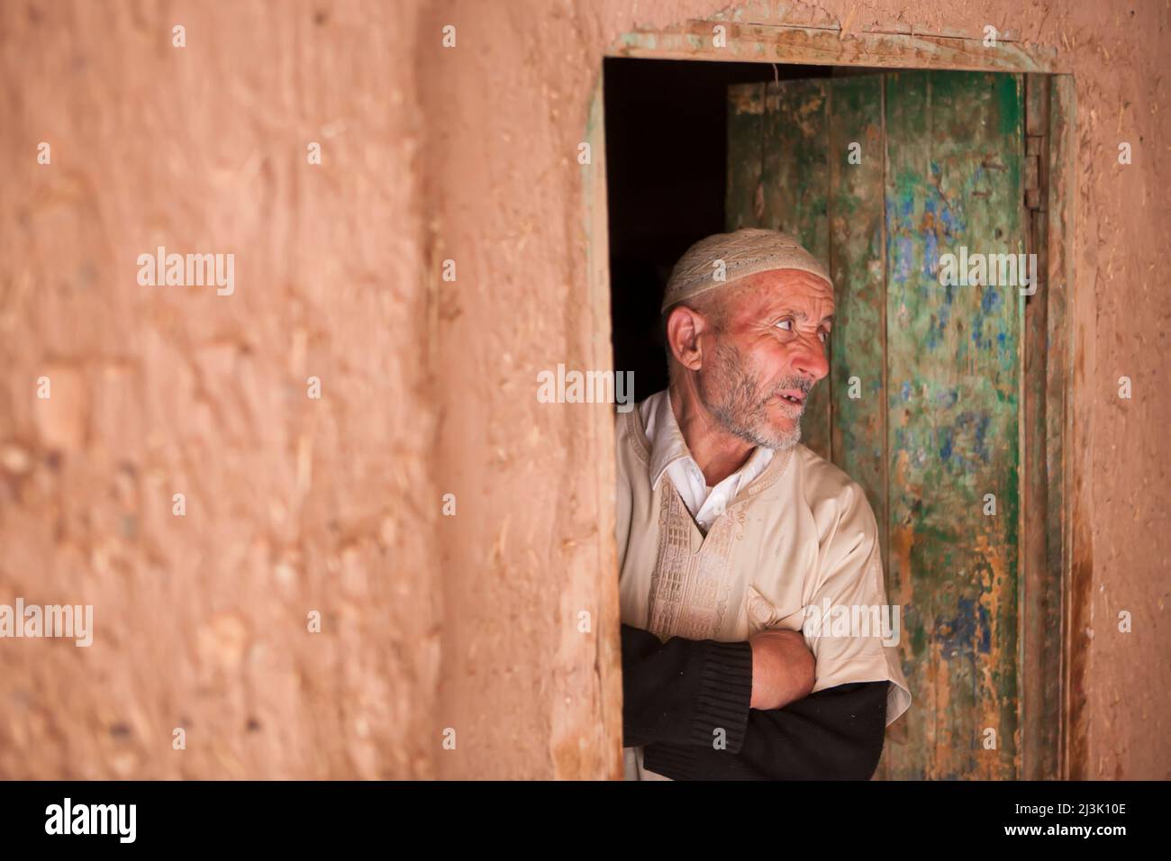 A mature man in traditional clothing stands in a doorway looking out in Ait Benhaddou, Morocco, a small village in the High Atlas Mountains where s... Stock Photo