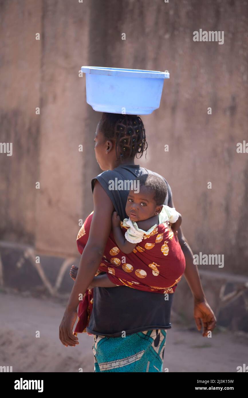 A Congolese woman with infant carries a plastic container on her head.; Kinshasa, Democratic Republic of the Congo. Stock Photo