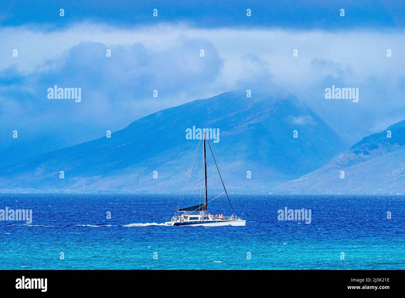 Sailboat moving through the vibrant blue water with the coastline of a hawaiian island in the distance Stock Photo