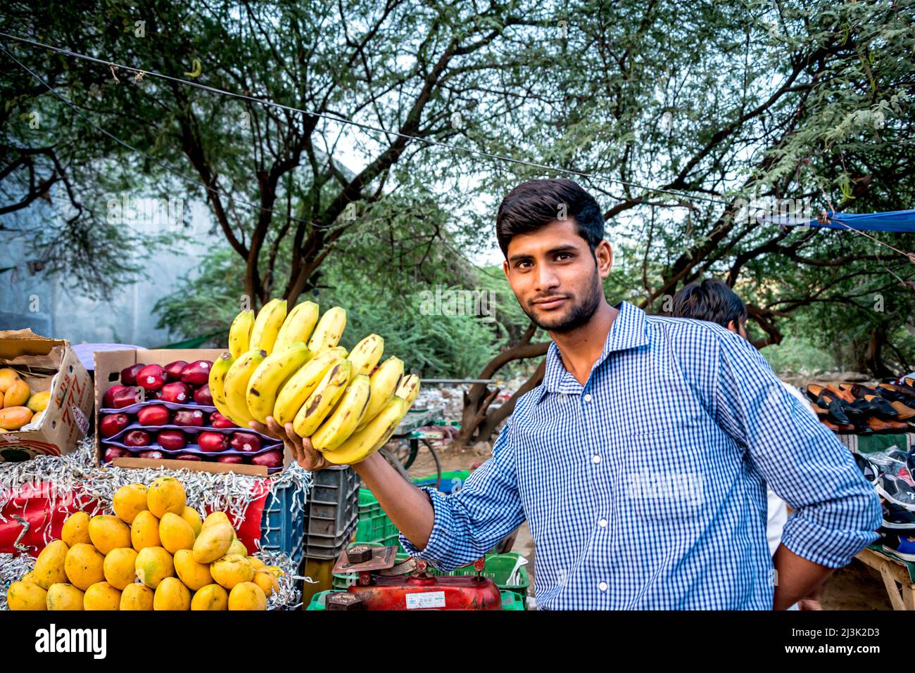 Young man holding a bundle of bananas at an outdoor fruit cart selling