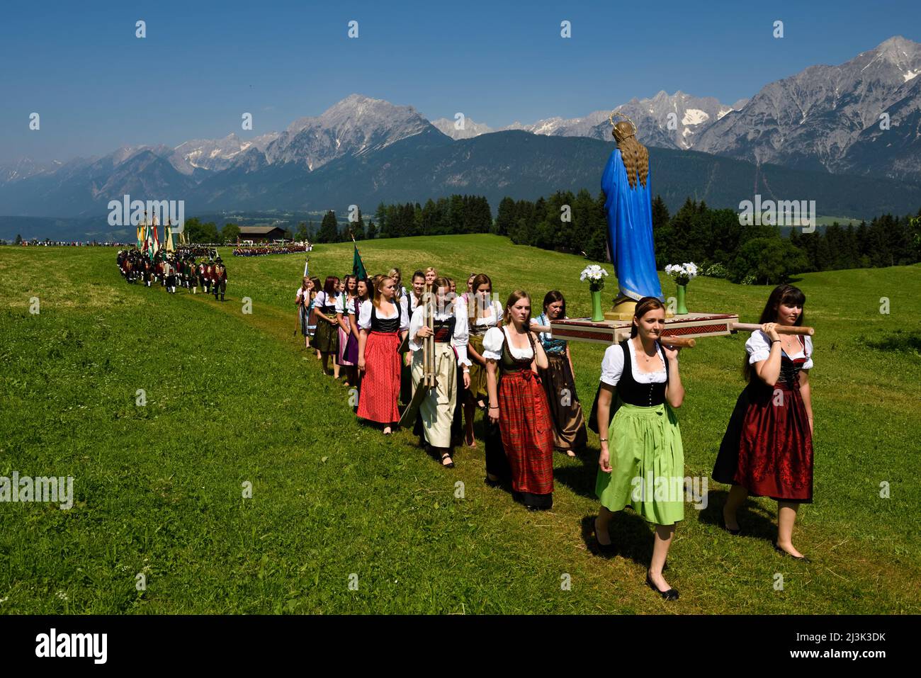 Leaving the village behind the procession enters a large meadow of grass overlooked by the mighty Karwendel mountain range. The Herz-Jesu festival was Stock Photo