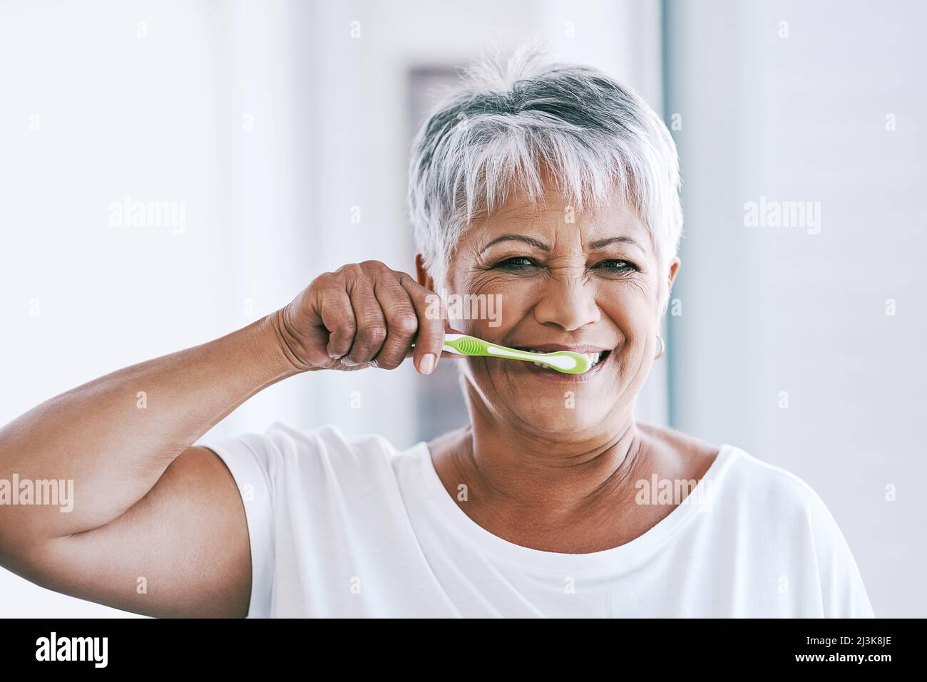 Early morning routines. Portrait of a cheerful mature woman brushing her teeth while looking at the camera at home. Stock Photo
