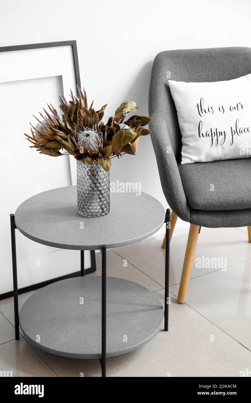 Stylish coffee table with dry flowers in vase and modern armchair near ...