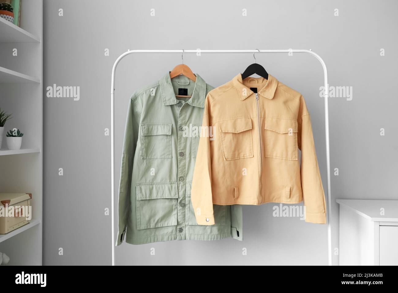 Rack with stylish jackets near light wall in room Stock Photo