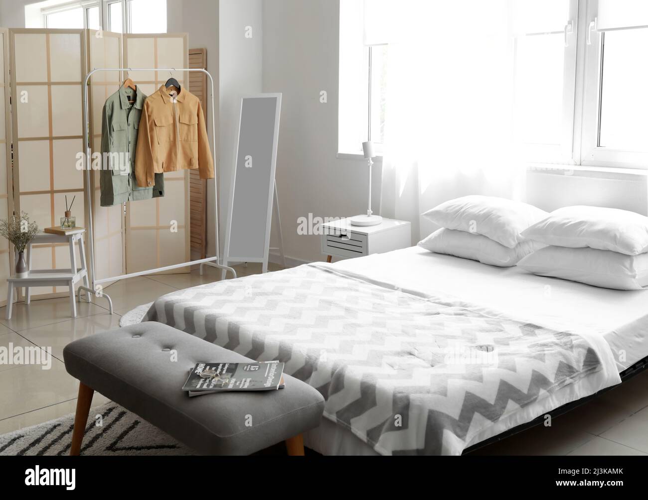Rack with stylish jackets near folding screen in bedroom Stock Photo
