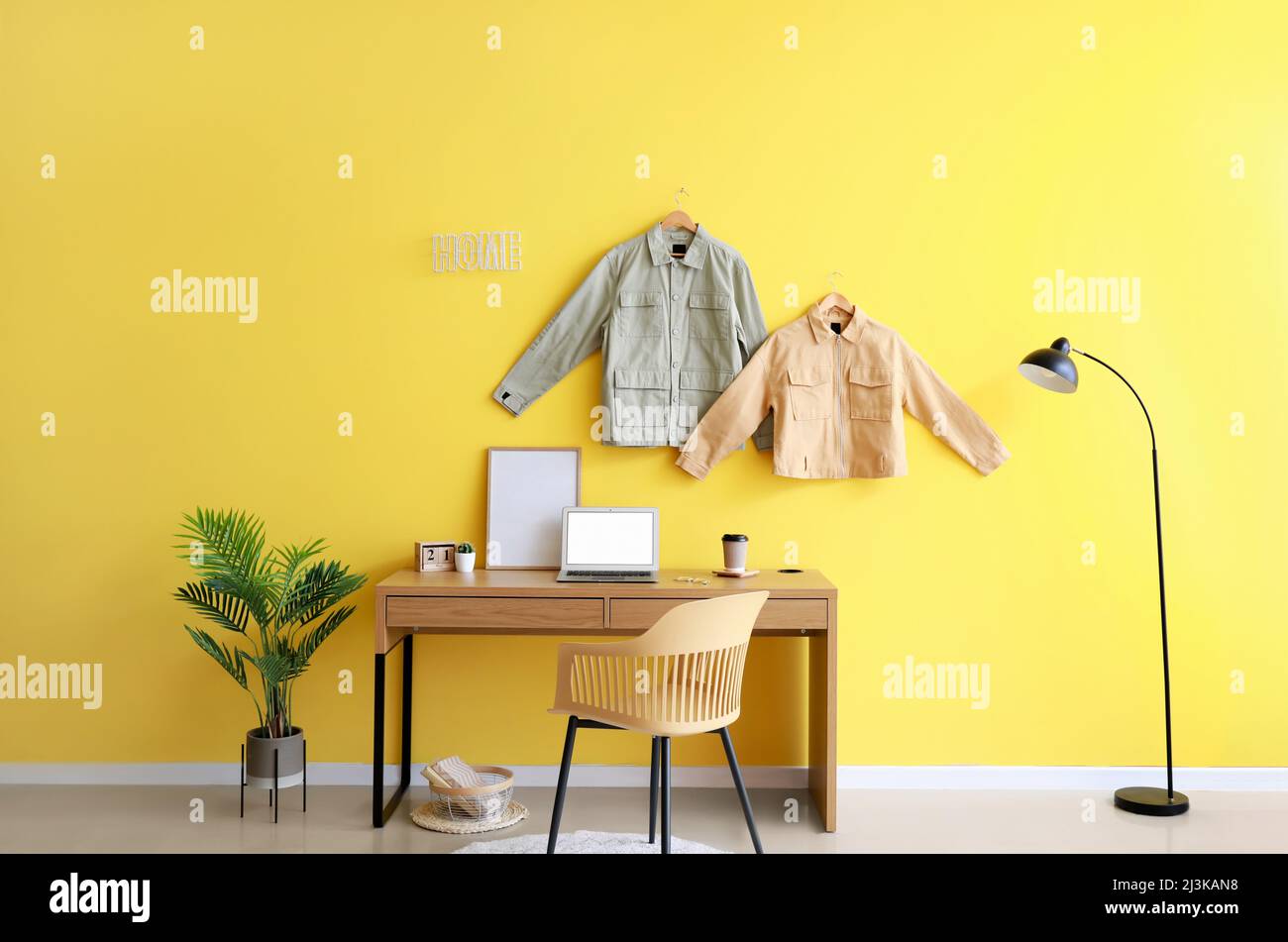 Interior of stylish room with modern workplace and stylish jackets hanging on color wall Stock Photo