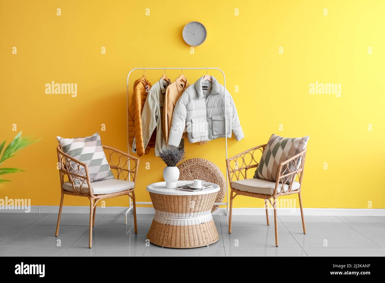 Interior of room with comfortable chairs and hanger with jackets near color wall Stock Photo