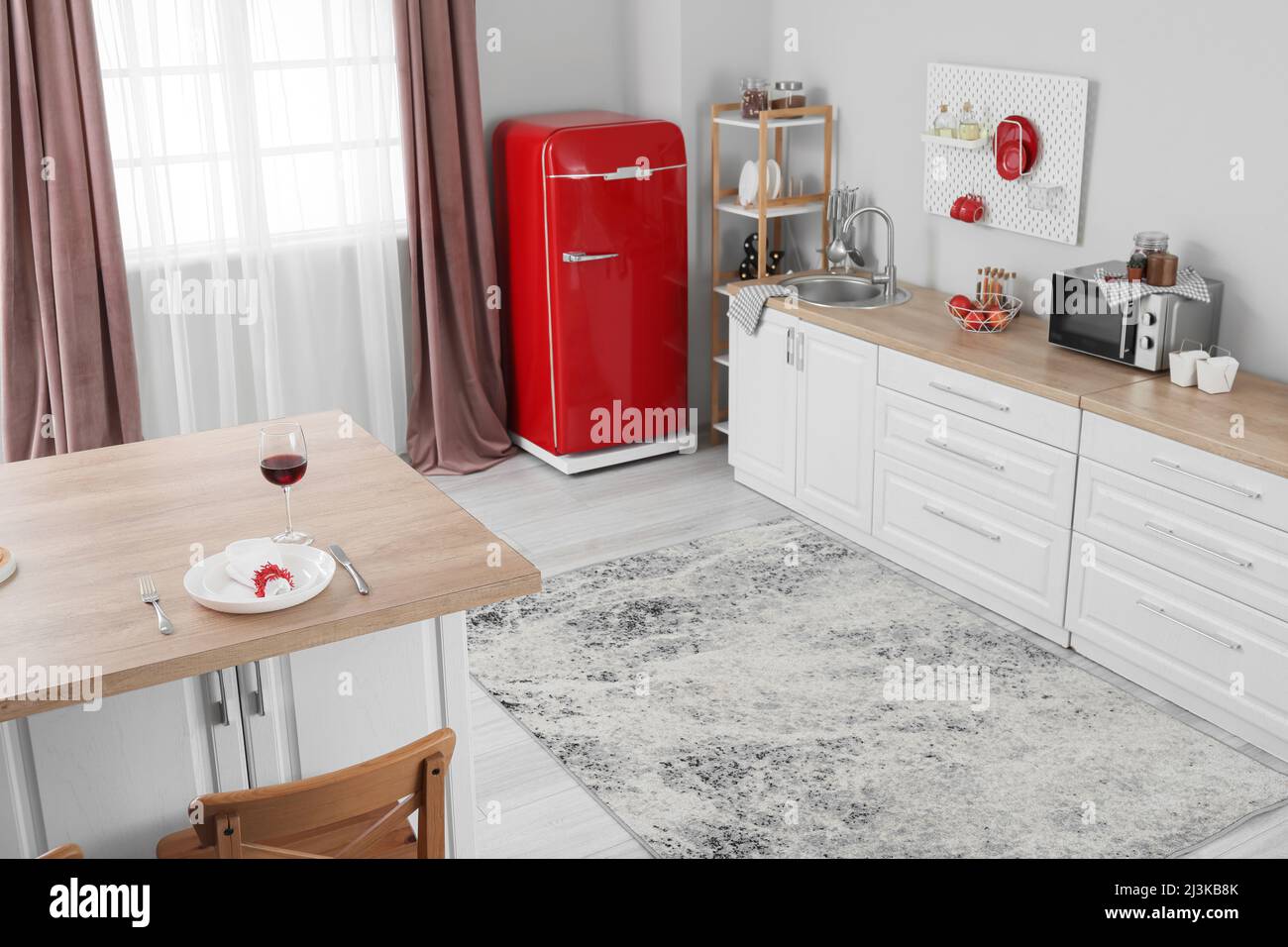 Interior of light kitchen with red fridge, white counters and pegboard