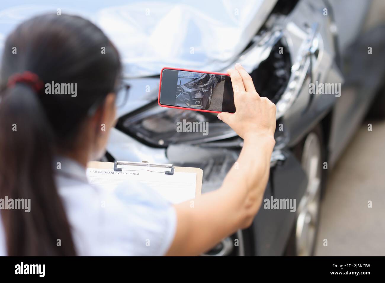 Agent takes smartphone photo of damage to car after accident Stock Photo