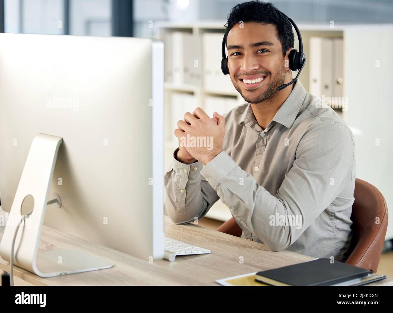 Day and night, we keep our customer service tight. Portrait of a young businessman using a headset and computer in a modern office. Stock Photo