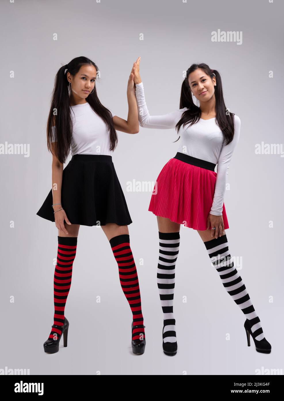 Two young brunette girl models with long bunches, wearing striped knee socks, black and red skirts and white blouses, posing and giving high-five. Ful Stock Photo
