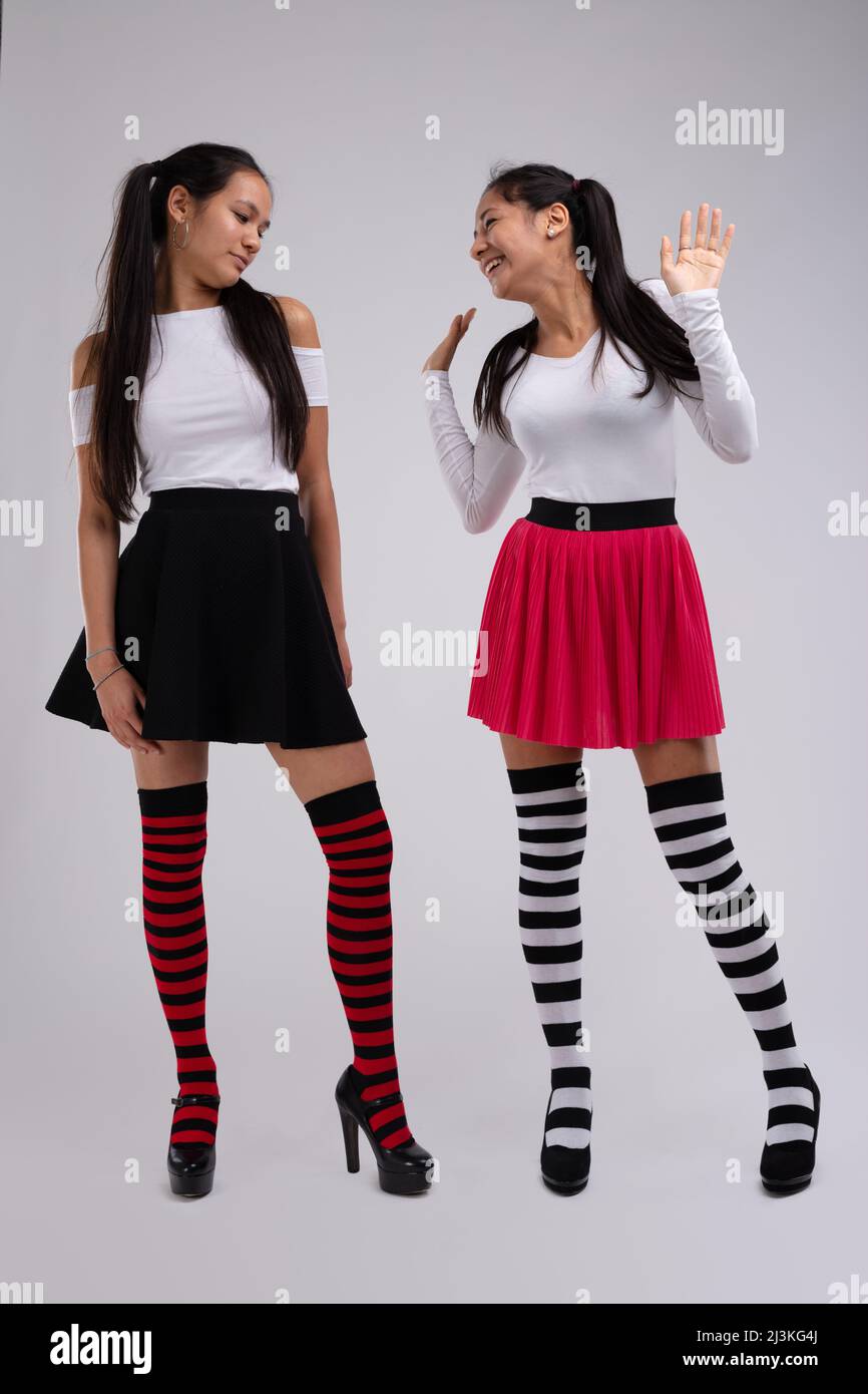 Young brunette girl looks appraisingly at her friend's outfit, that looks similar to hers. Both models wear funny striped knee socks, black and red sk Stock Photo