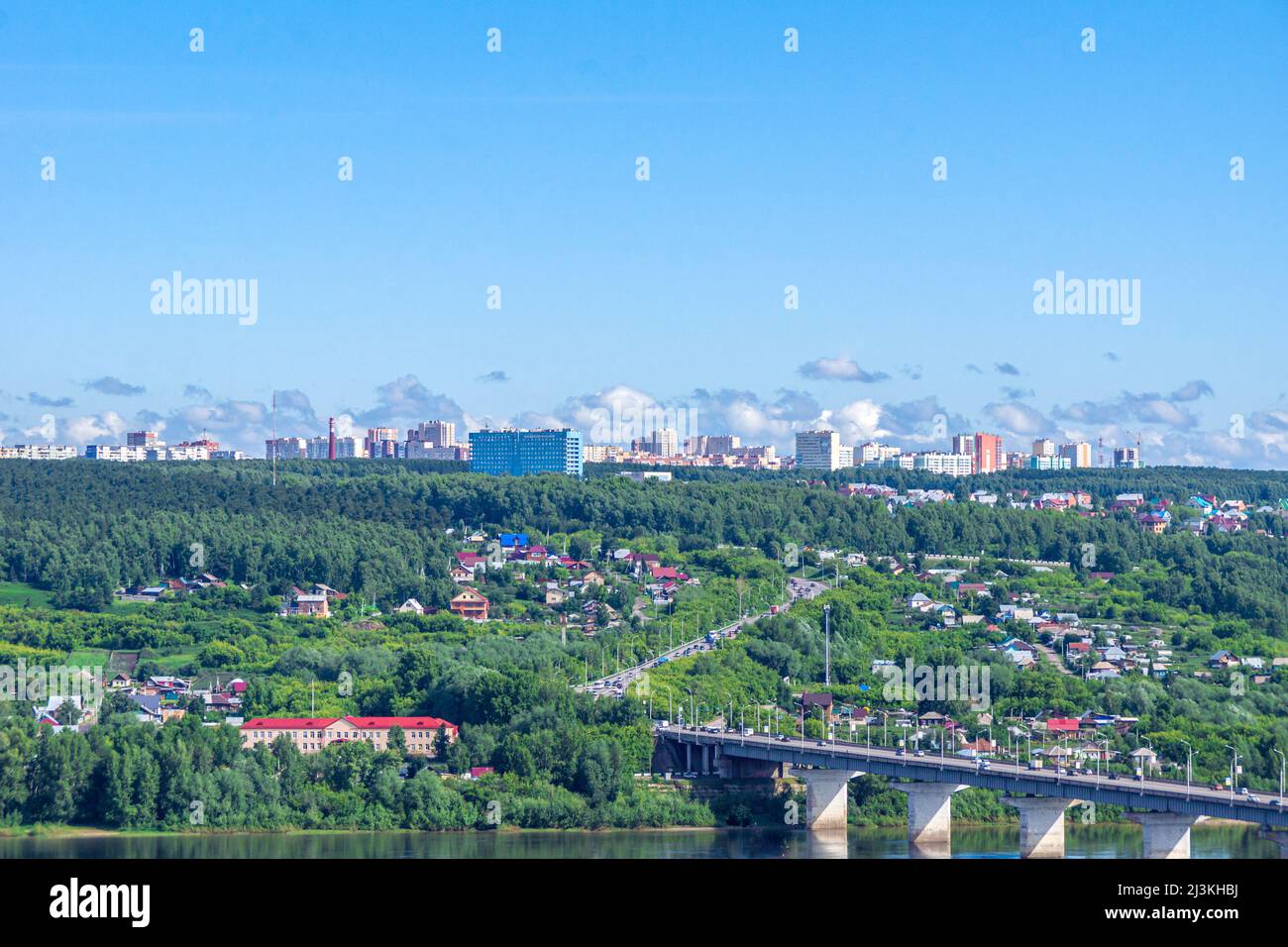 Kemerovo, Russia - June 24, 2021. Suburban village houses on shore and multi-storey residential buildings behind a forest on a hill, in foreground a r Stock Photo