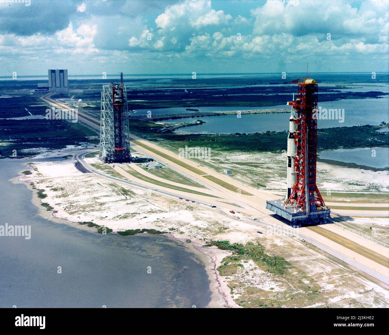 The Apollo 4 launch vehicle (right) is rolled out from the Vehicle Assembly Building (left), August 26, 1967. The Mobile Servicing Structure is towards center. Stock Photo