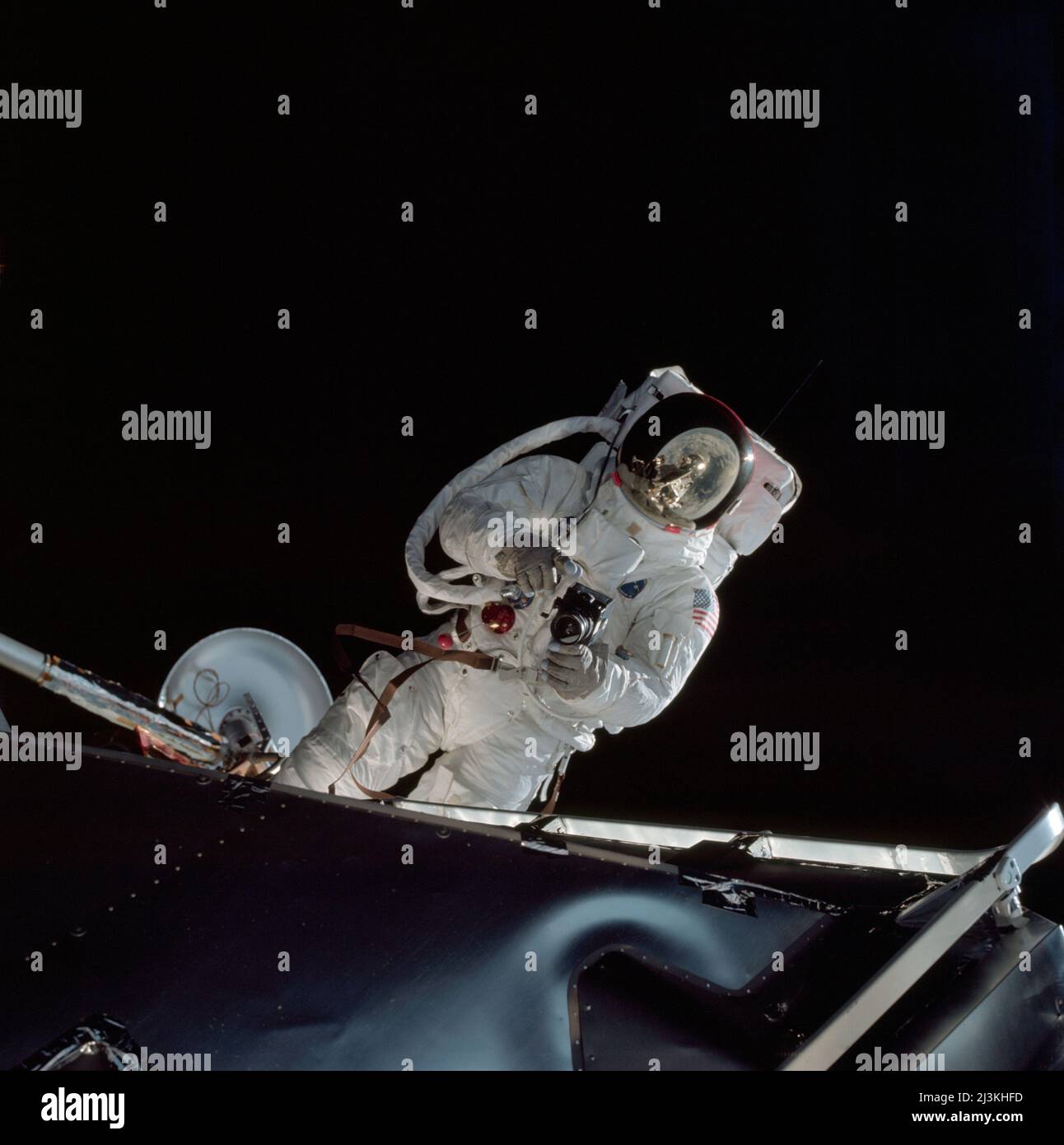 Astronaut Russell Schweickart,taking photos during a spacewalk during teh Apollo 9 mission.  Schweickart, wearing an Extravehicular Mobility Unit (EMU), is standing in 'golden slippers' on the Lunar Module porch. On his back, partially visible, are a Portable Life Support System (PLSS) and an Oxygen Purge System (OPS). Stock Photo