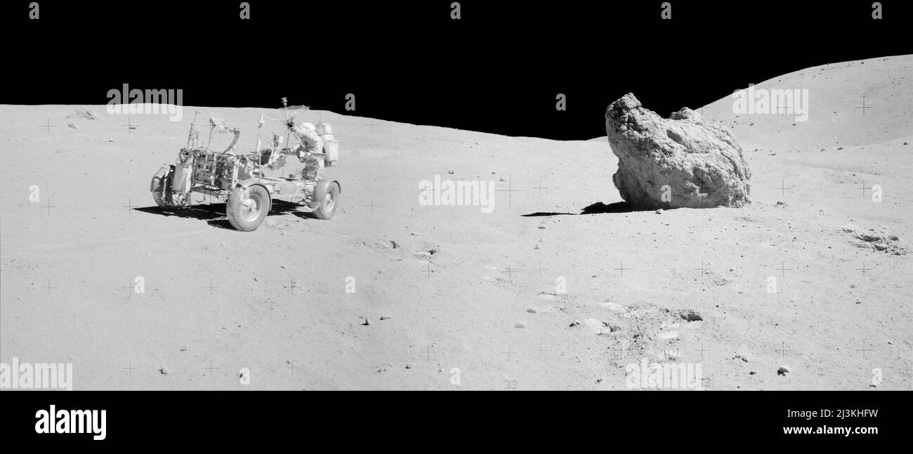 Mission Apollo 16:  John Young aiming the high-gain antenna at the Earth prior to sending TV signals. Shadow Rock at right and Smoky Mountain behind it. The stop at station 13 was to collect a series of samples from a permanently shadowed area. Shadow Rock, a 4-m-diameter boulder to the right in the photograph, was the location of the sampling. Stock Photo