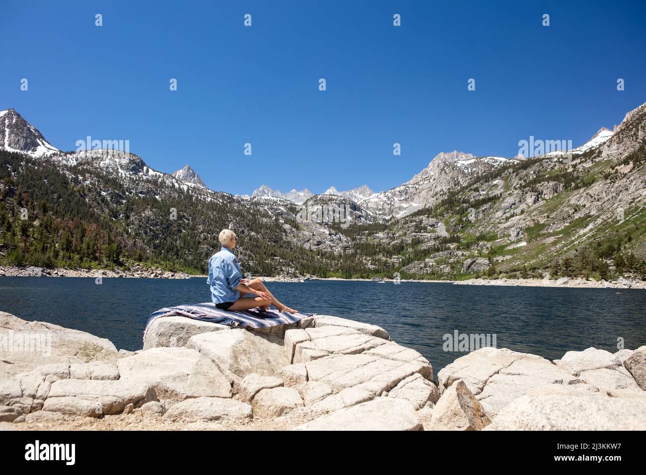 A woman sits by an alpine lake in the Sierra Nevadas. Stock Photo