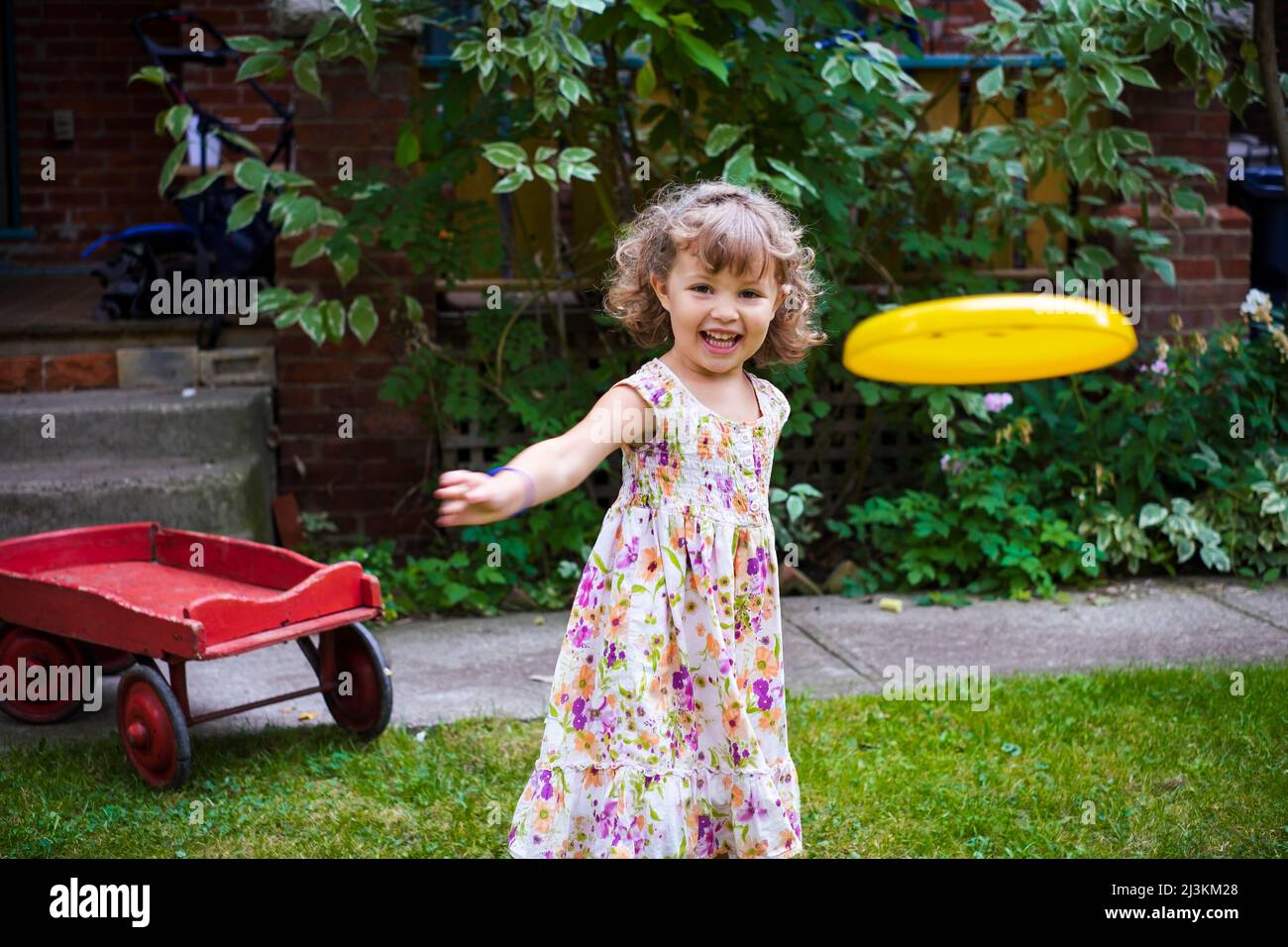 Preschooler girl throwing a frisbee towards the camera in her yard at home; Toronto, Ontario, Canada Stock Photo