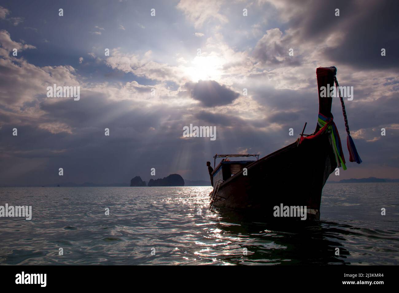 A man leans off of a long tail boat in the Andaman sea under rays of light. Stock Photo
