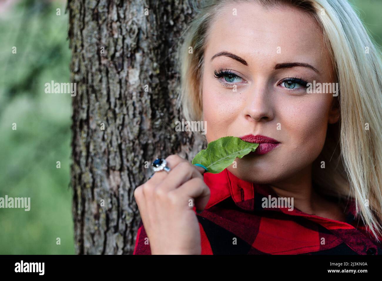 Pensive Young Woman Chewing On A Green Leaf As She Relaxes Leaning On