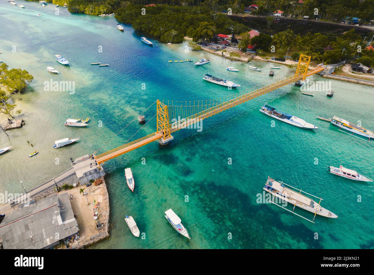 Aerial of boats on the waterway passing under the iconic Yellow Bridge connecting Nusa Lembongan and Nusa Ceningan Stock Photo