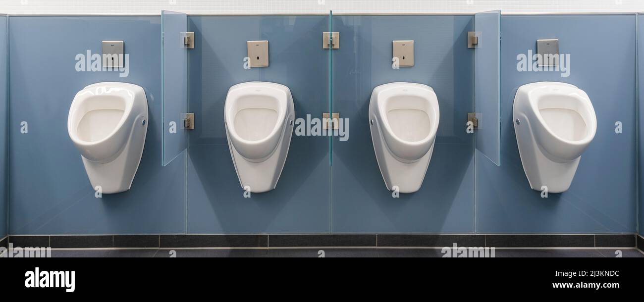 Four white urinals in a row on a blue wall in a men's restroom at the