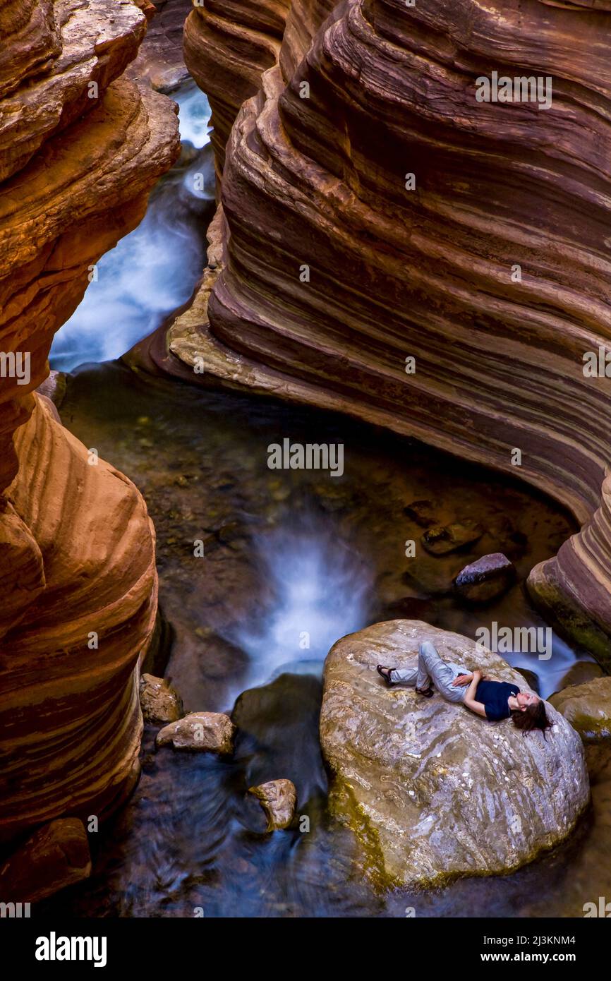 A hiker relaxing on a large rock in a slot canyon at the Colorado River Mile 136 in the Arizona Cascades along Deer Creek Stock Photo