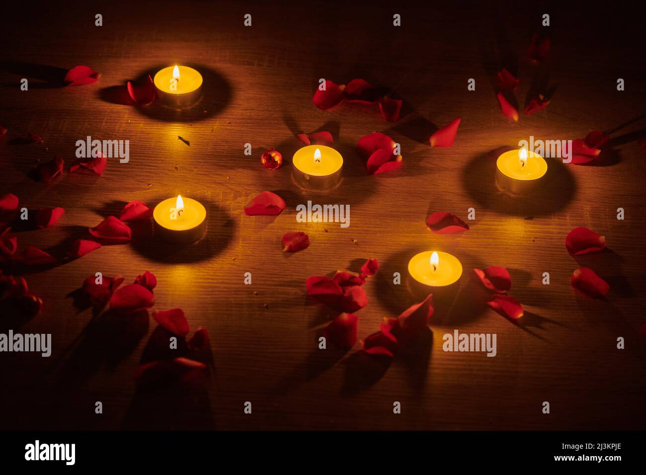 Illuminated tealight candles and red rose petals scattered on a surface create a romantic setting; Studio Stock Photo