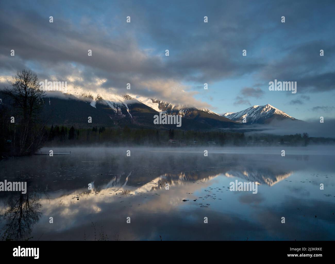 Rugged peak of Hudson Bay Mountain covered in snow with mist rising off the lake in the foreground at sunrise; Smithers, British Columbia, Canada Stock Photo