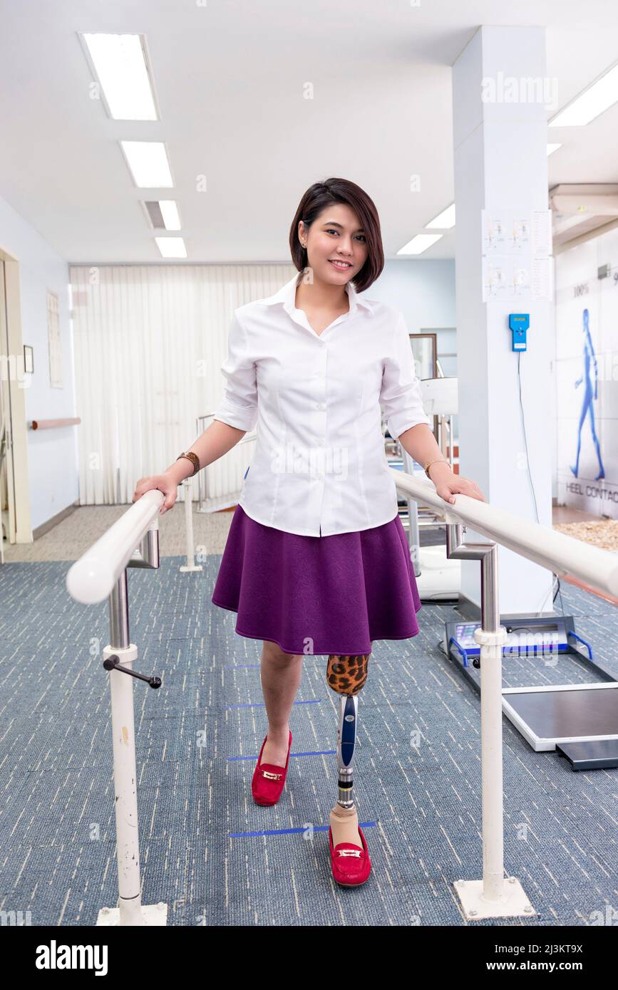 Young woman with leg prosthesis in therapy, walking with handrails; Bangkok, Thailand Stock Photo