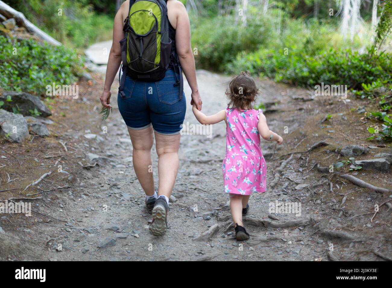Mother and young daughter hold hands and walk down a trail on a hike together in Smuggler Cove Marine Provincial Park along the Sunshine Coast of B... Stock Photo