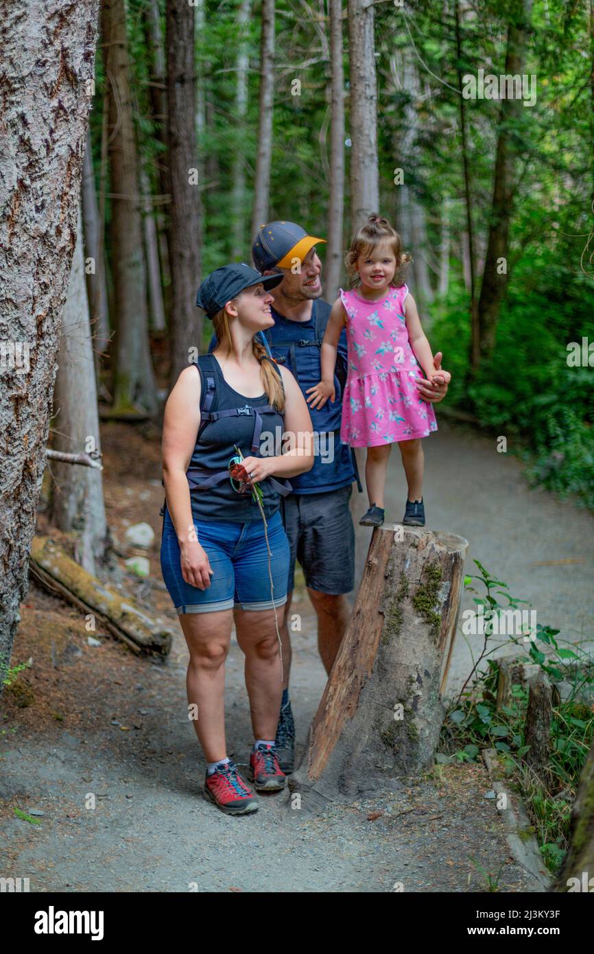 Young family holding hands and walking down a trail on a hike together in Smuggler Cove Marine Provincial Park along the Sunshine Coast of BC, Canada Stock Photo