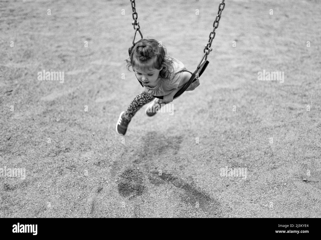 Black and white image of a preschooler girl laying across a swing on her belly swinging; West Vancouver, British Columbia, Canada Stock Photo
