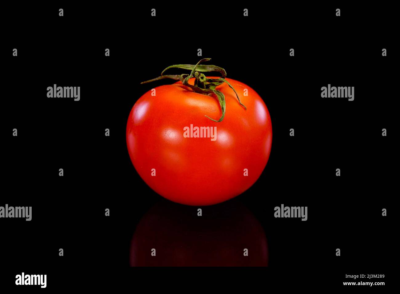 Red tomato on a black background. Fresh and firm tomato. Restaurant, groceries store or agriculture promo. Stock Photo