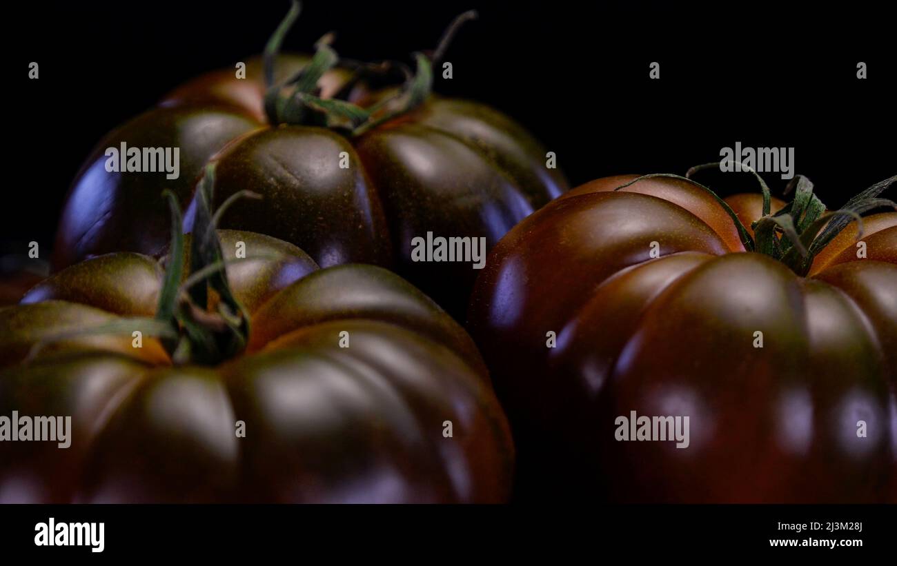 Chocolate tomatoes on a black background, close up view. Fresh and firm tomato. Restaurant, groceries store or agriculture promo. Stock Photo