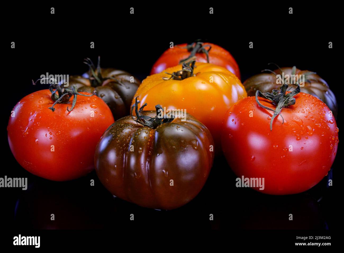 Different kinds of tomatoes on a black background. Fresh and firm tomato. Restaurant, groceries store or agriculture promo. Stock Photo