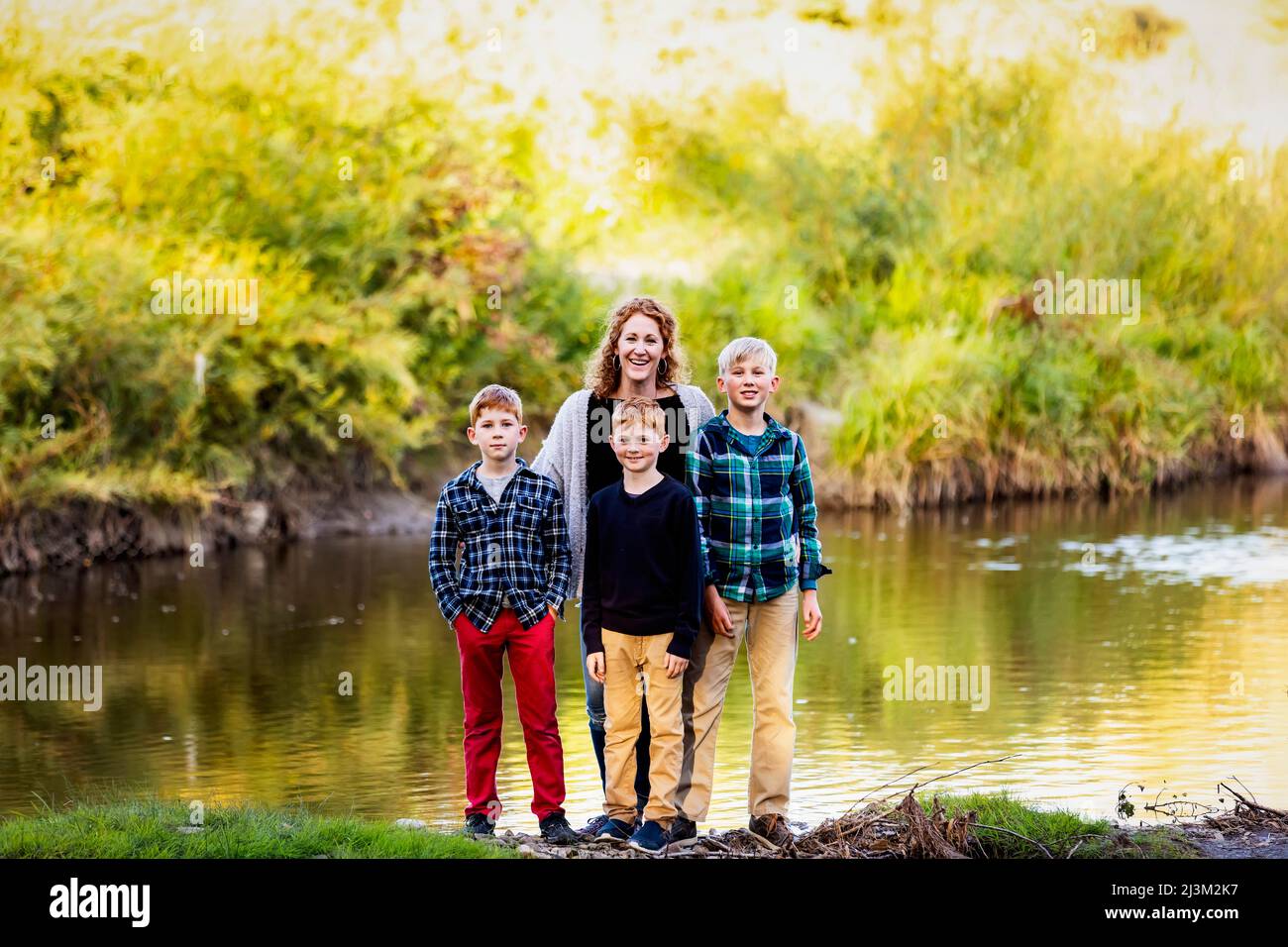 Portrait of a mother with three boys standing at the water's edge in a park in autumn; Edmonton, Alberta, Canada Stock Photo
